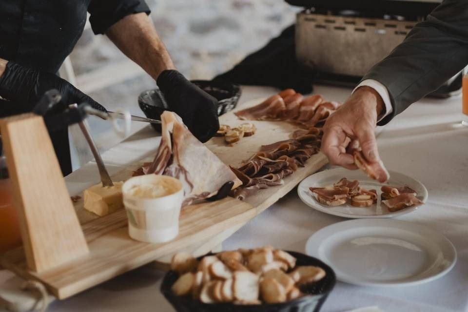 Des mains gantées tranchent du jambon sur une planche en bois, au buffet d’une réception