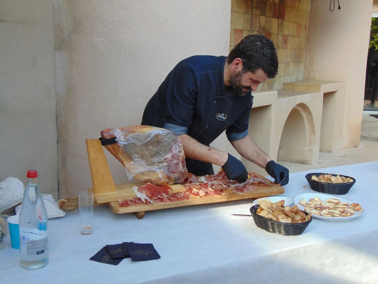 Le chef tranche un jambon à la main, sur un buffet dressé en plein air