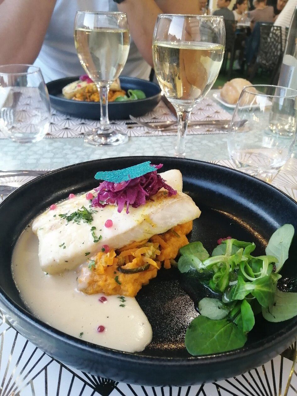 Filet de poisson blanc sur une purée orangée et des légumes en julienne, sauce blanche, chou rouge et mâche, dans une assiette creuse noire