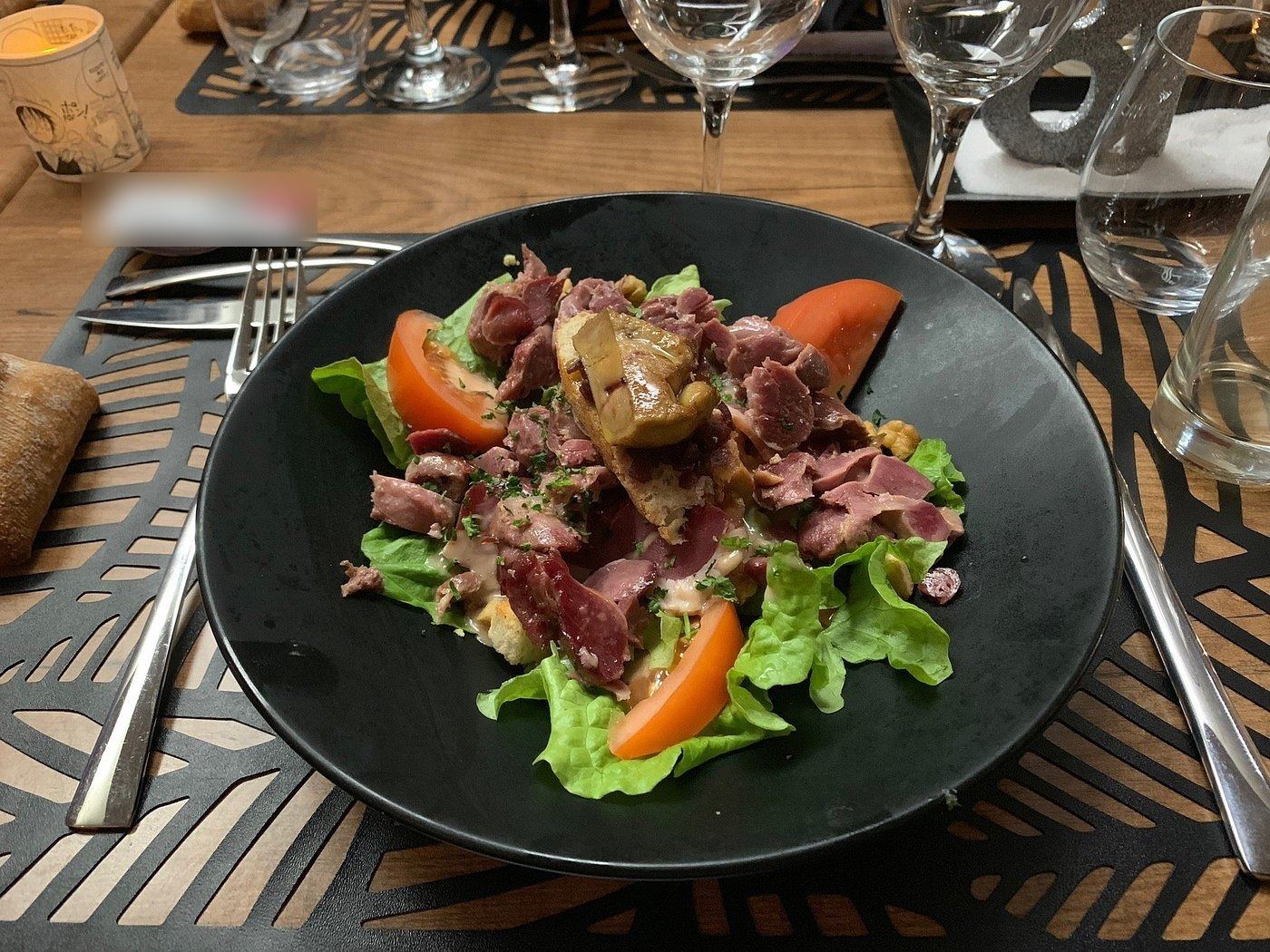 Salade gourmande aux gésiers, tomates et salade verte, dans une assiette noire