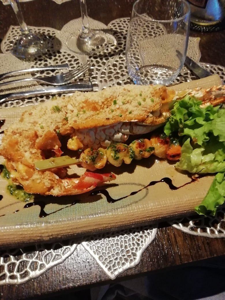 Demi-langouste gratinée et sa brochette de fruits de mer, servie avec une salade verte