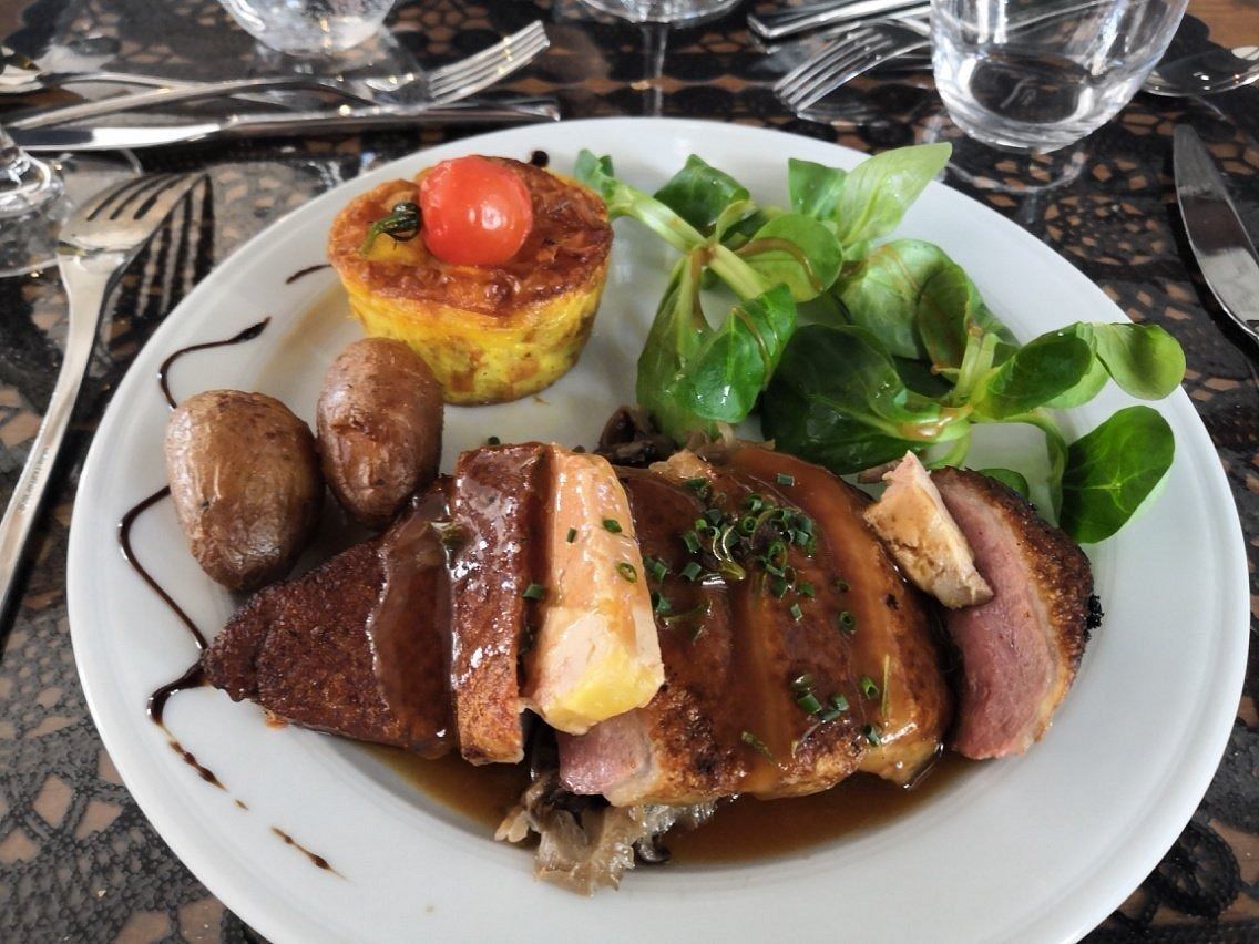 Magret de canard tranché et nappé de sauce, pommes grenaille, petit flan surmonté d’une tomate cerise et mâche, dans une assiette blanche