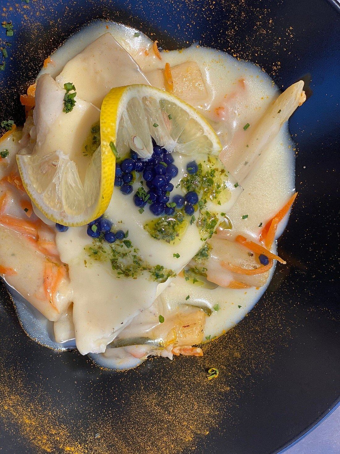 Plat nappé d’une sauce blanche, perles bleues, rondelle de citron torsadée et julienne de carottes, dans une assiette creuse sombre