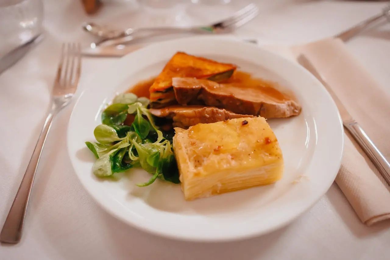 Tranches de rôti nappées de jus, gratin de pommes de terre et mâche, dans une assiette blanche