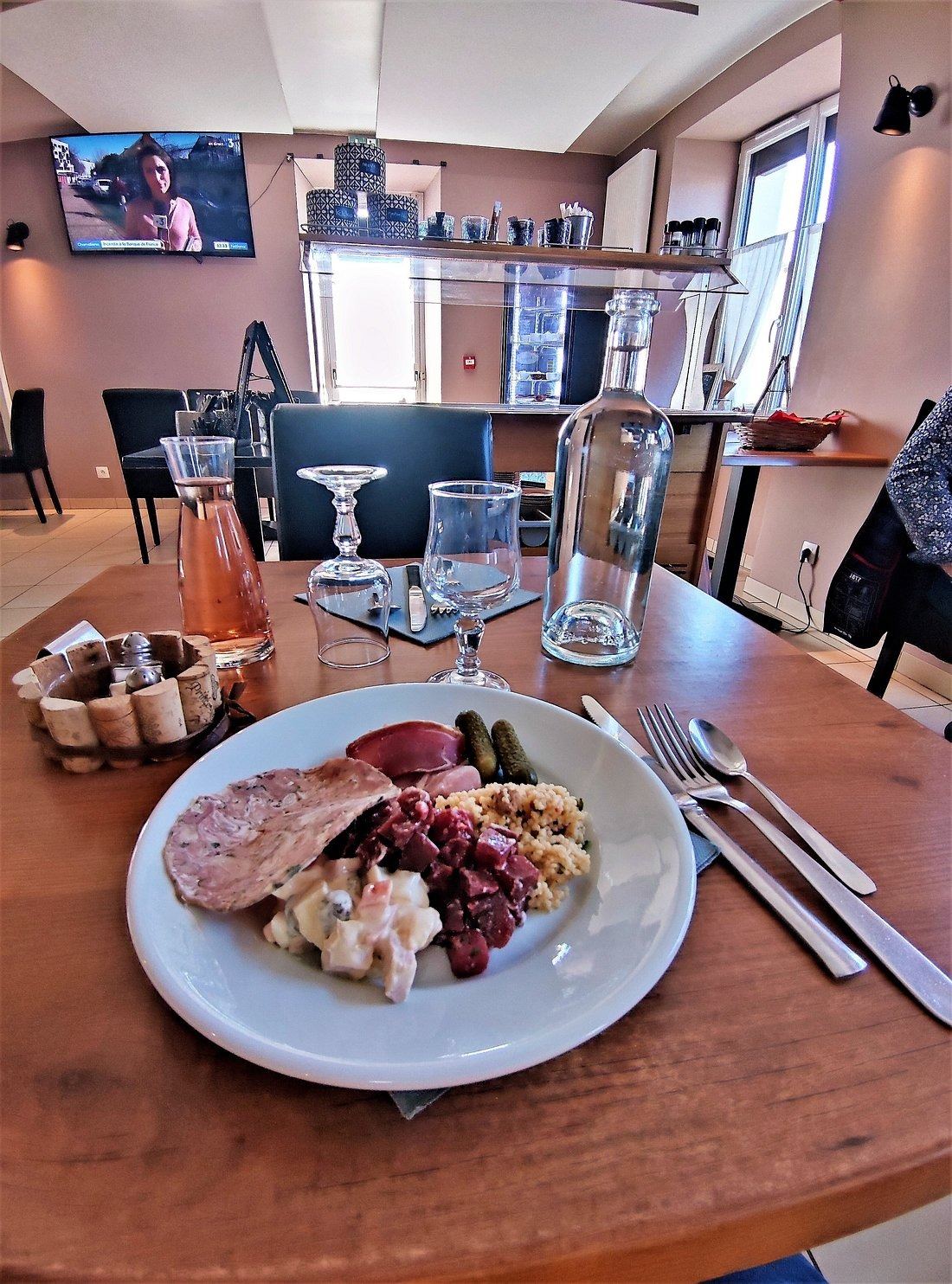 Assiette de terrine, salades composées et cornichons, sur une table en bois, dans la salle du restaurant